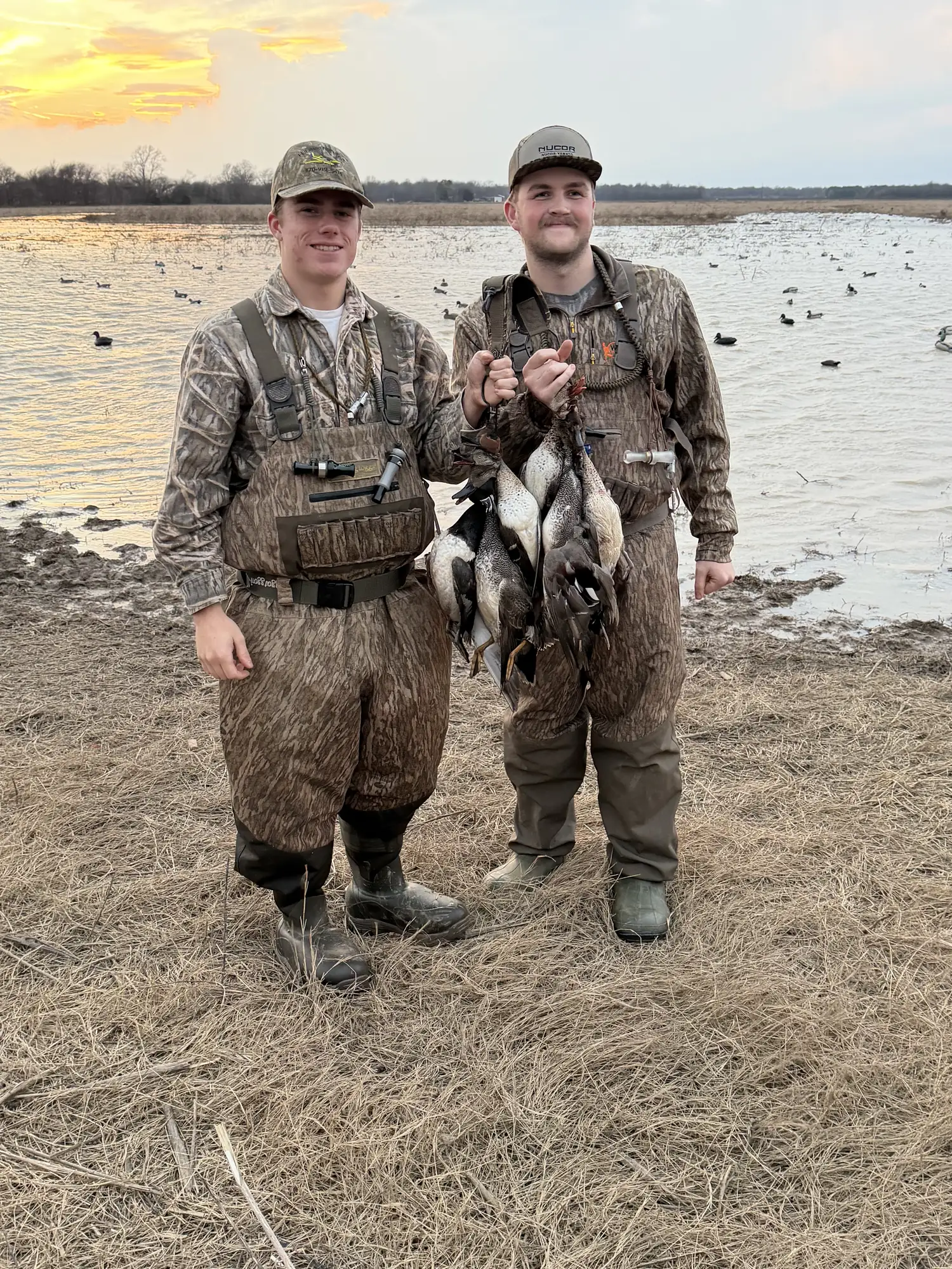 Two hunters at sunrise on the water's edge holding drake mallards